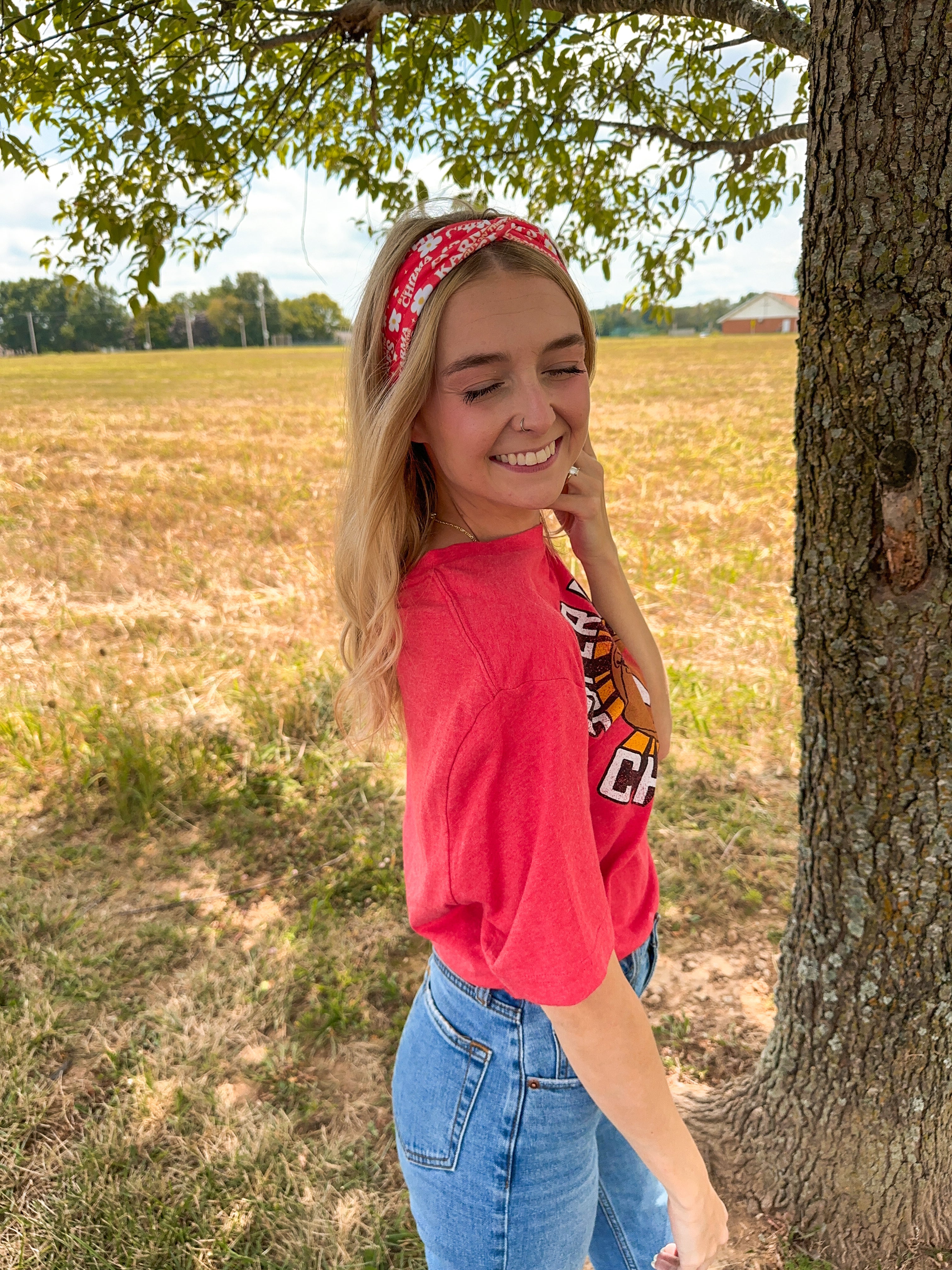 Woman smiling in a red Karma Is the Guy on the Chiefs headband, showcasing its versatile, functional design for workouts, long shifts, or playdays.