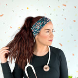 Woman wearing Beautiful Day to Catch Babies Lilac Market Headband with stethoscope, exuding confidence and style.