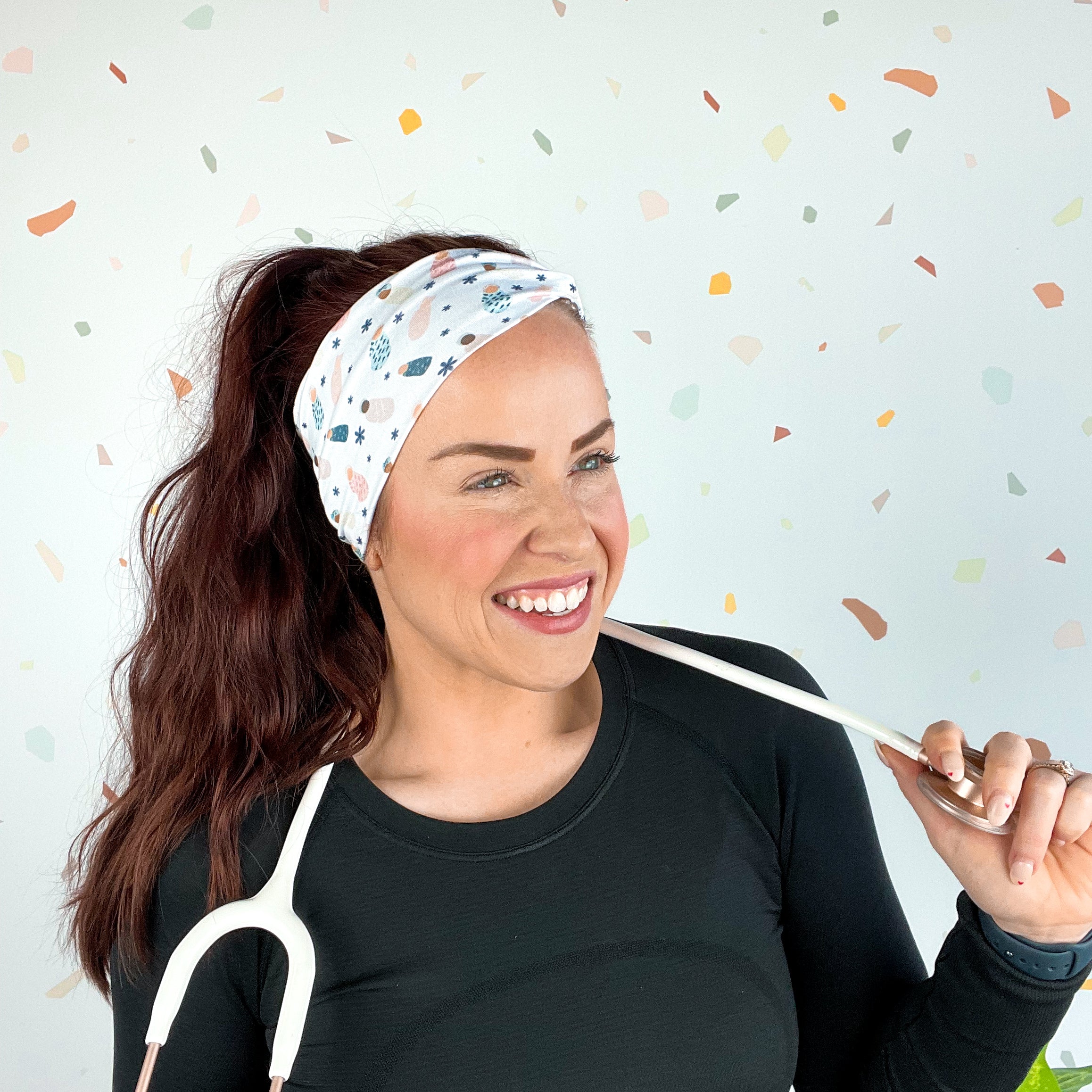 A woman wearing the Ask Me About Our Burritos headband with a stethoscope, smiling.