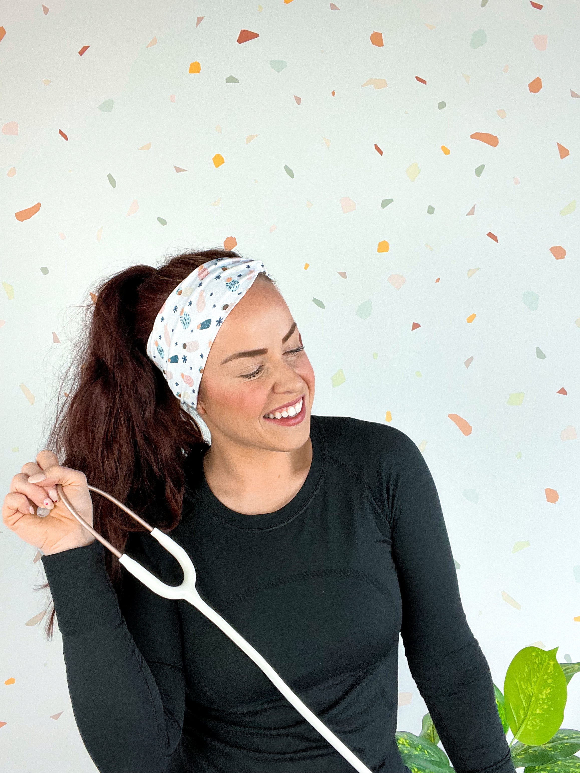 A woman wearing the Ask Me About Our Burritos headband with a stethoscope, smiling.