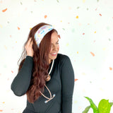 Woman wearing We Deliver Headband, smiling confidently with stethoscope around neck.