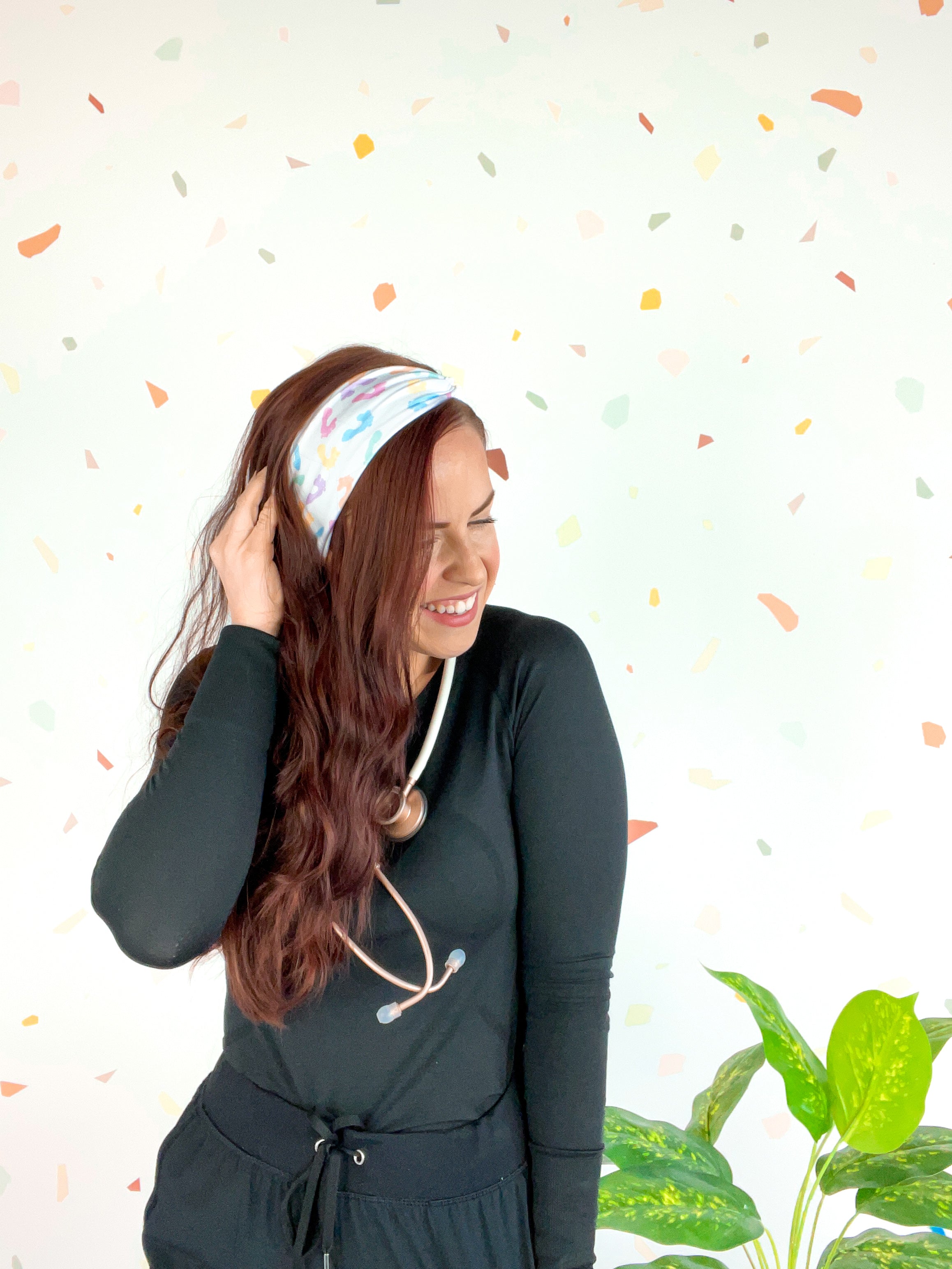 Woman wearing We Deliver Headband, smiling confidently with stethoscope around neck.