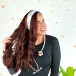 Woman wearing We Deliver Headband, smiling confidently with stethoscope around neck.