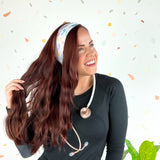 Woman wearing We Deliver Headband, smiling confidently with stethoscope around neck.