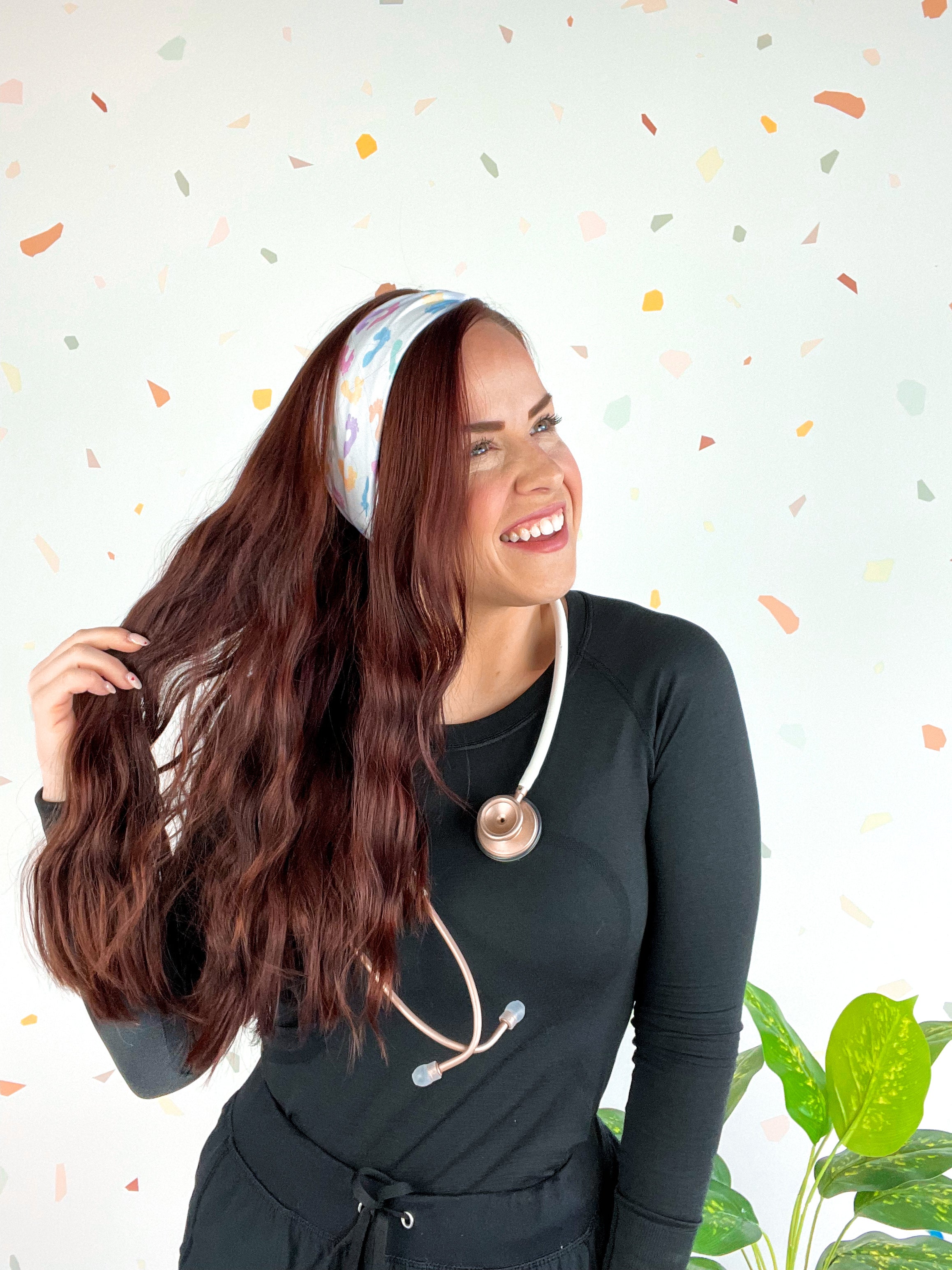 Woman wearing We Deliver Headband, smiling confidently with stethoscope around neck.