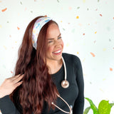 Woman wearing We Deliver Headband, smiling confidently with stethoscope around neck.