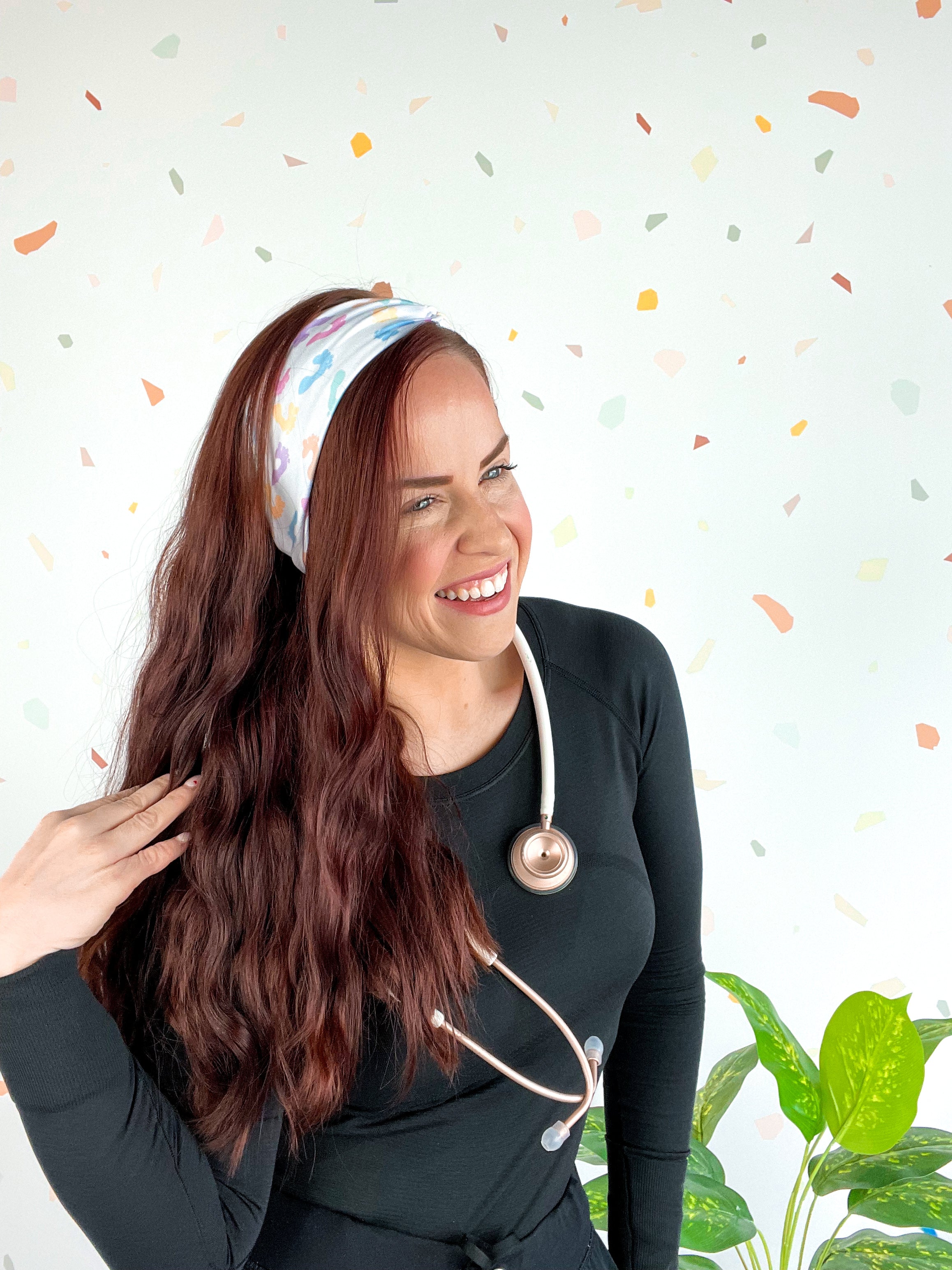 Woman wearing We Deliver Headband, smiling confidently with stethoscope around neck.