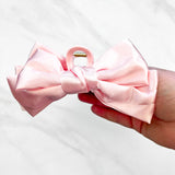 A hand holding a Classy Chic Lilac Clip, a perfect claw clip for all hair types and textures, made of silky pink satin material with a hinge closure.