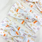 Adult women's white headband with stacked and upright books, and allover daisies and stars in pastels