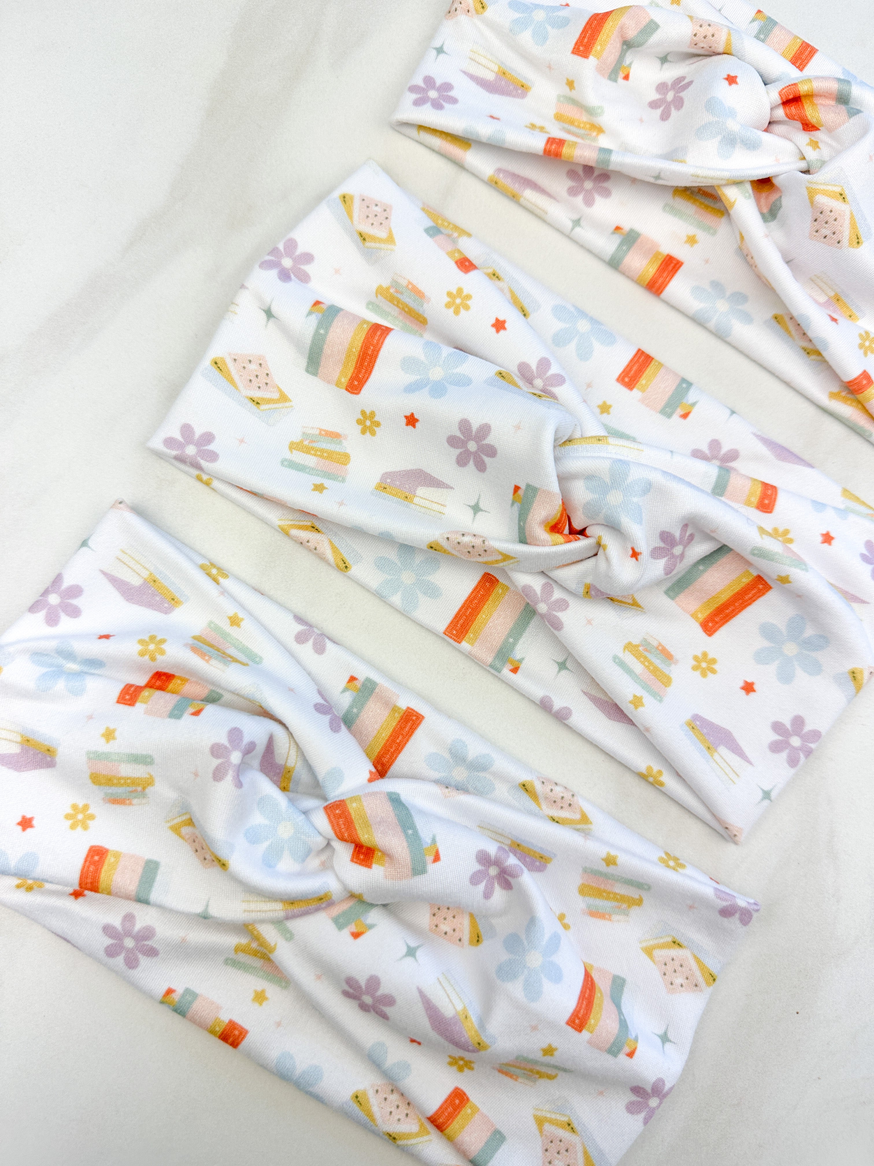 Adult women's white headband with stacked and upright books, and allover daisies and stars in pastels