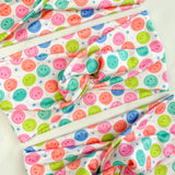Adult women's white headband with bright purple, pink, teal, coral and purple smiley faces and tiny stars