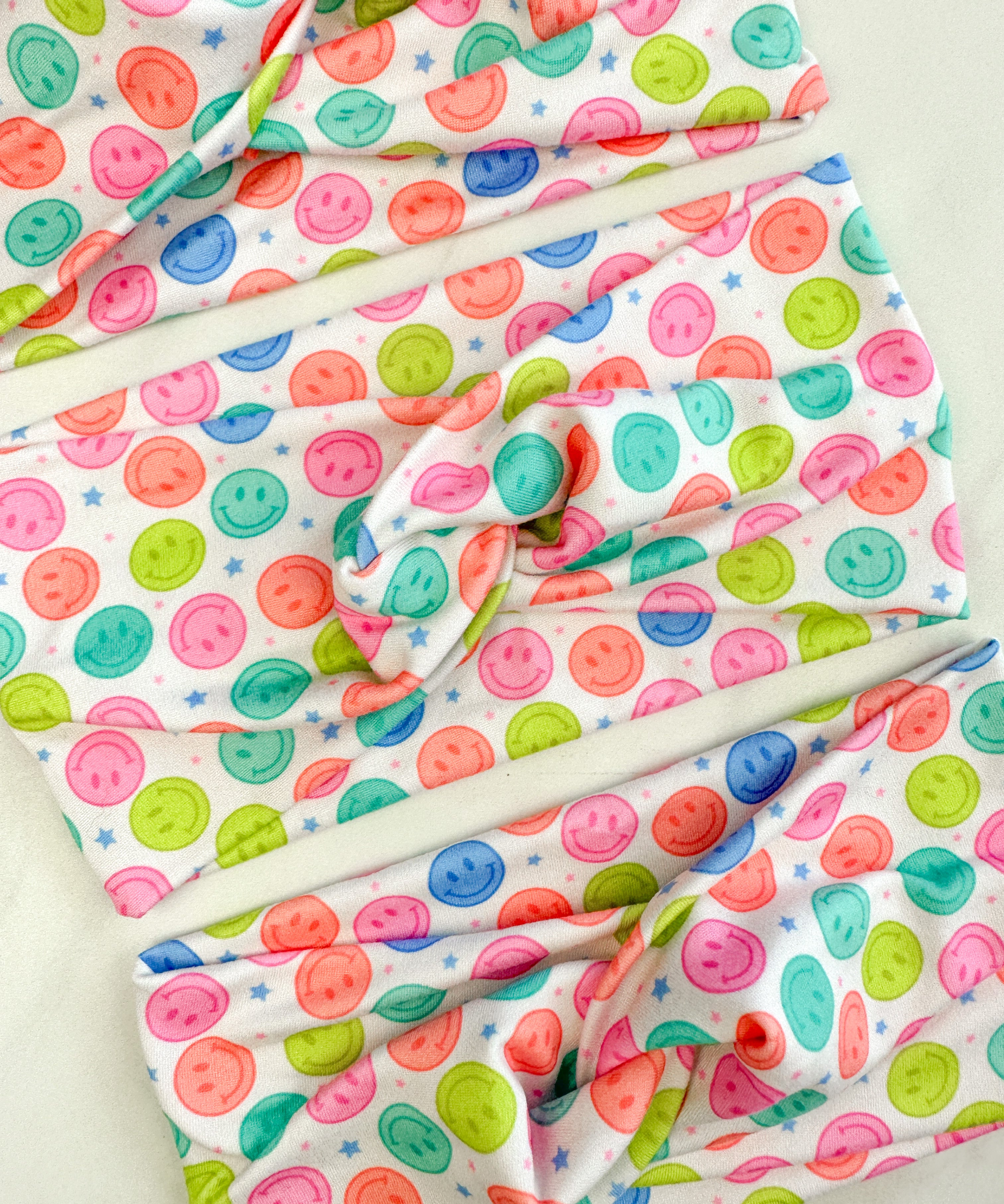 Adult women's white headband with bright purple, pink, teal, coral and purple smiley faces and tiny stars