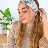 A woman wearing a Lilac Market Brandi Floral on Mint headband, showcasing a white and tan floral print design. Versatile 3-in-1 twist style, sweat absorbent, non-slip, machine washable, designed in Springfield, MO.