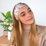 A woman wearing the Alyssa Floral on Ivory headband, showcasing a versatile twist style. Made of soft, stretchy fabric, sweat-absorbent, and non-slip for workouts or play. Designed in Springfield, MO.