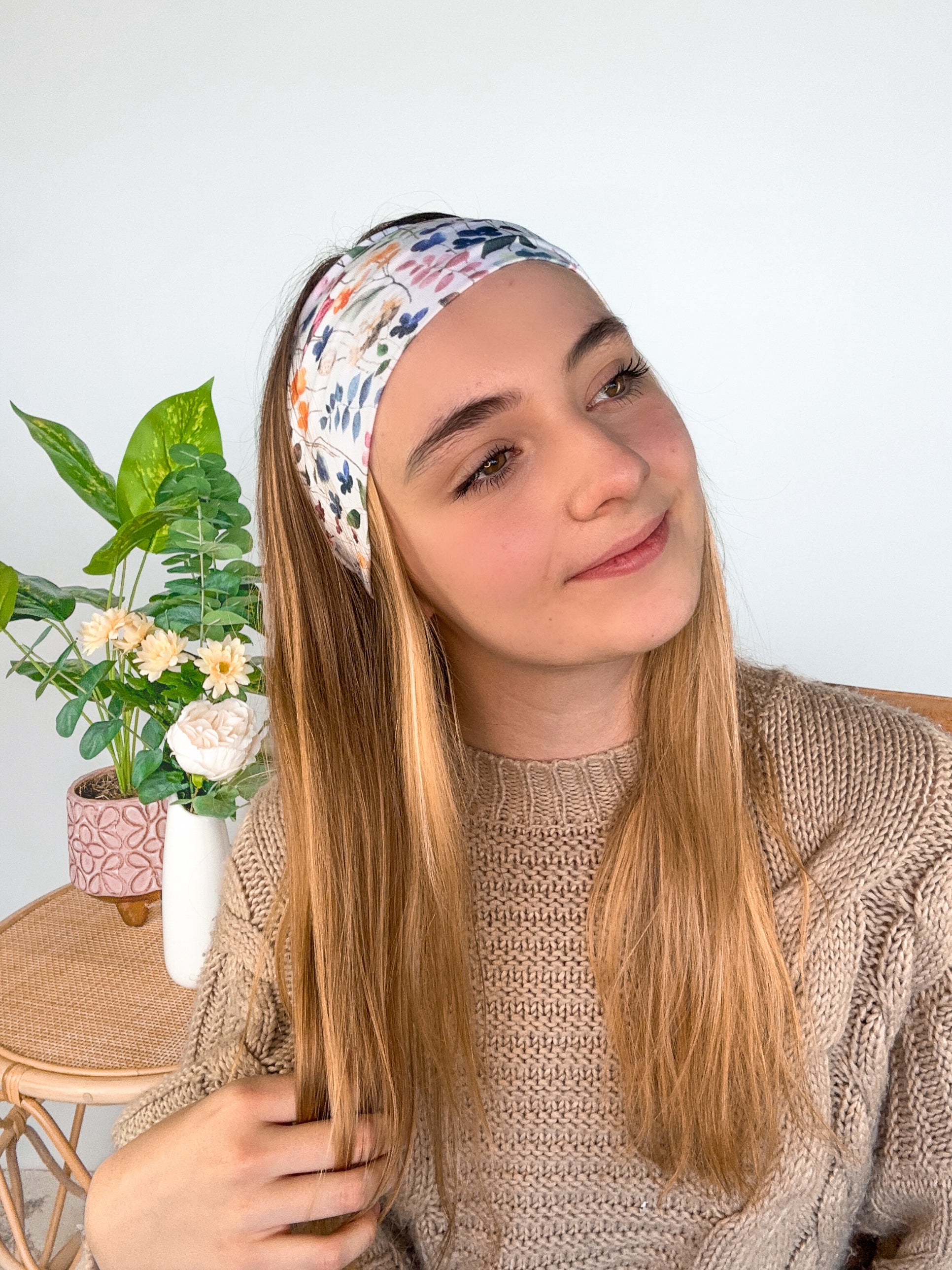 A woman wearing the Alyssa Floral on Ivory headband, showcasing a versatile twist style. Made of soft, stretchy fabric, sweat-absorbent, and non-slip for workouts or play. Designed in Springfield, MO.