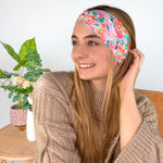 A woman smiling wearing a Kara Floral on Blue headband, showcasing a versatile 3-in-1 twist style. Functional, machine washable, sweat-absorbent, and non-slip for workouts or play. Designed in Springfield, MO.