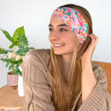 A woman smiling wearing a Kara Floral on Blue headband, showcasing a versatile 3-in-1 twist style. Functional, machine washable, sweat-absorbent, and non-slip for workouts or play. Designed in Springfield, MO.