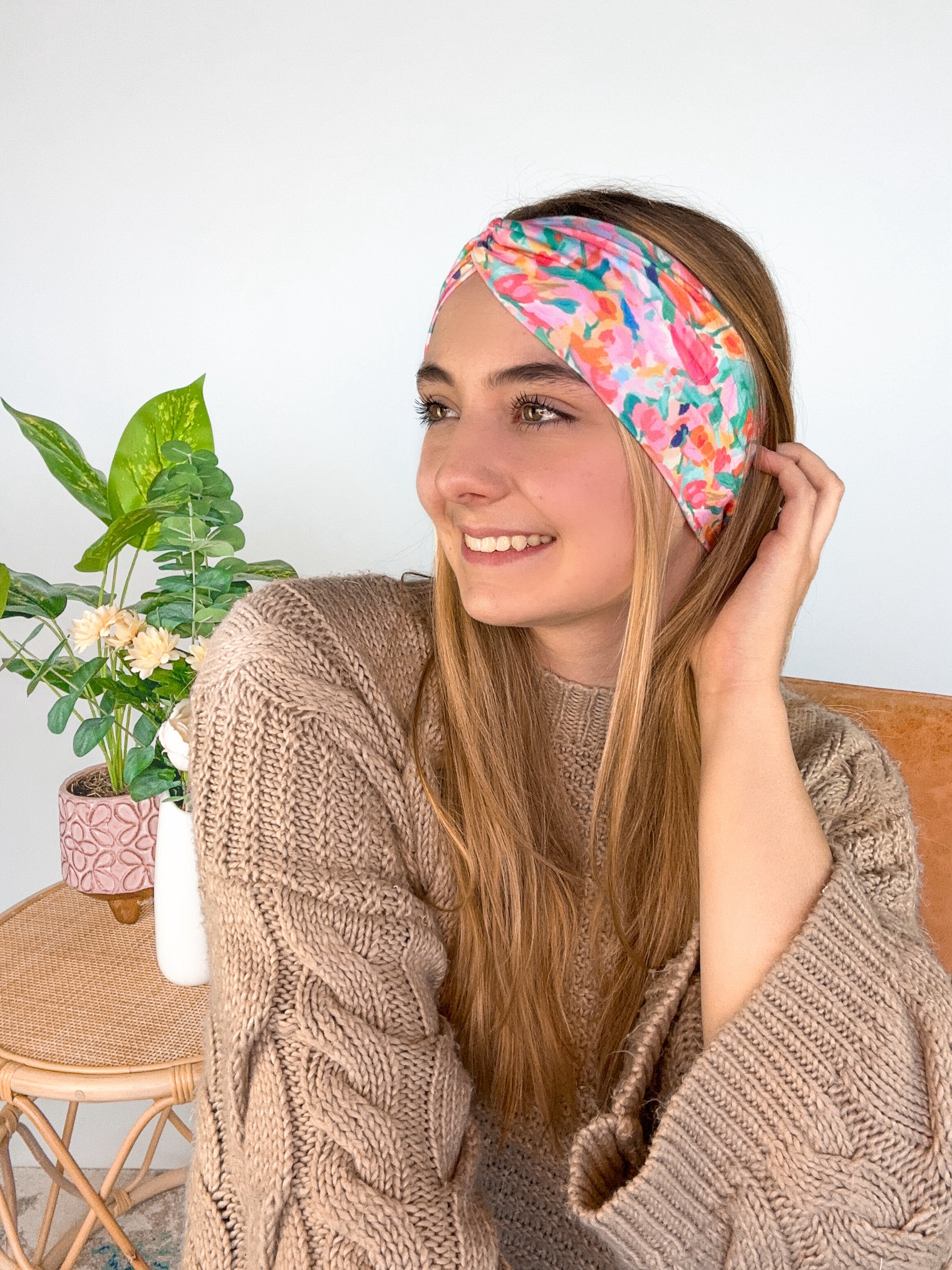 A woman smiling wearing a Kara Floral on Blue headband, showcasing a versatile 3-in-1 twist style. Functional, machine washable, sweat-absorbent, and non-slip for workouts or play. Designed in Springfield, MO.