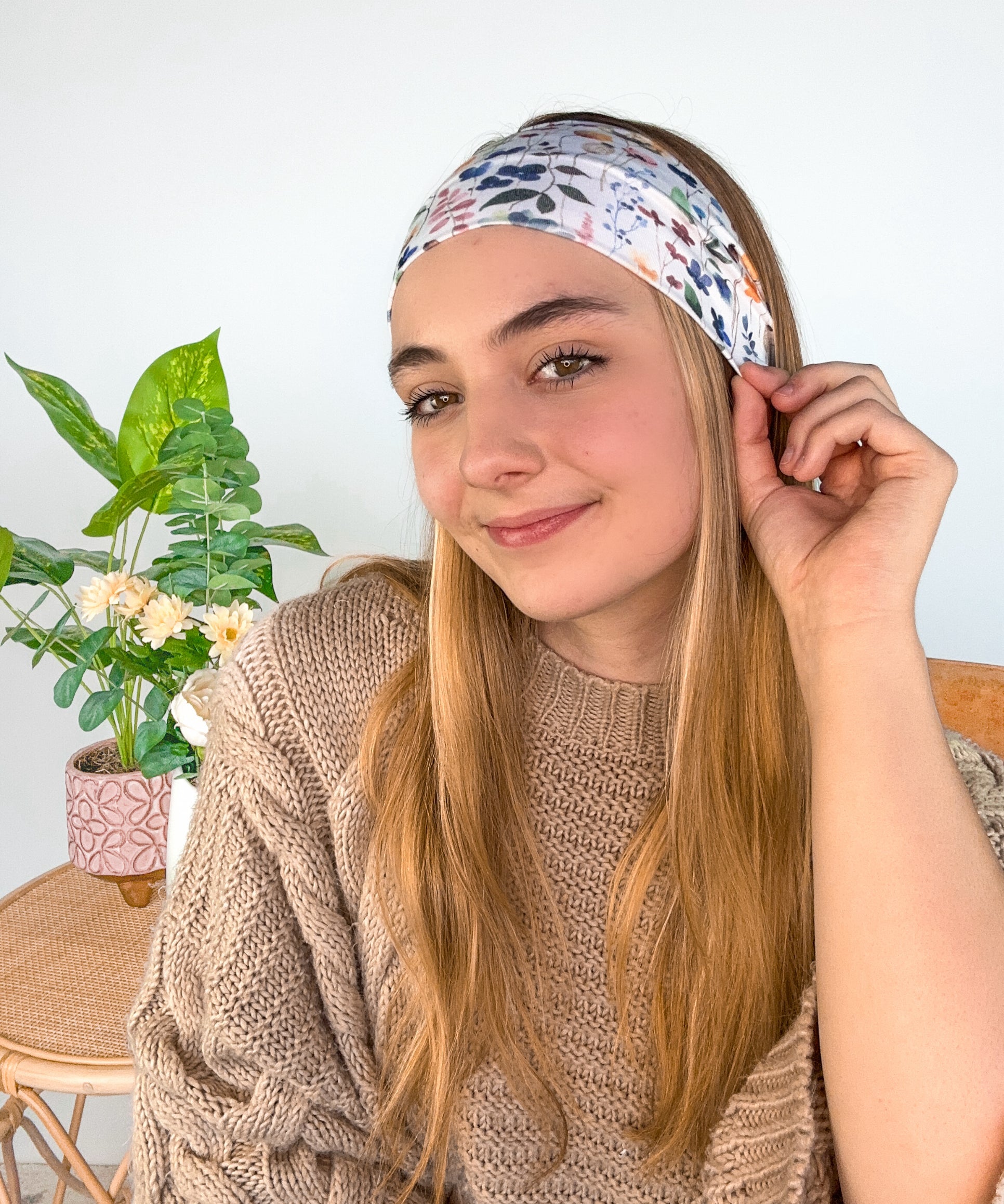 A woman wearing the Alyssa Floral on Ivory headband, showcasing a versatile twist style. Made of soft, stretchy fabric, sweat-absorbent, and non-slip for workouts or play. Designed in Springfield, MO.