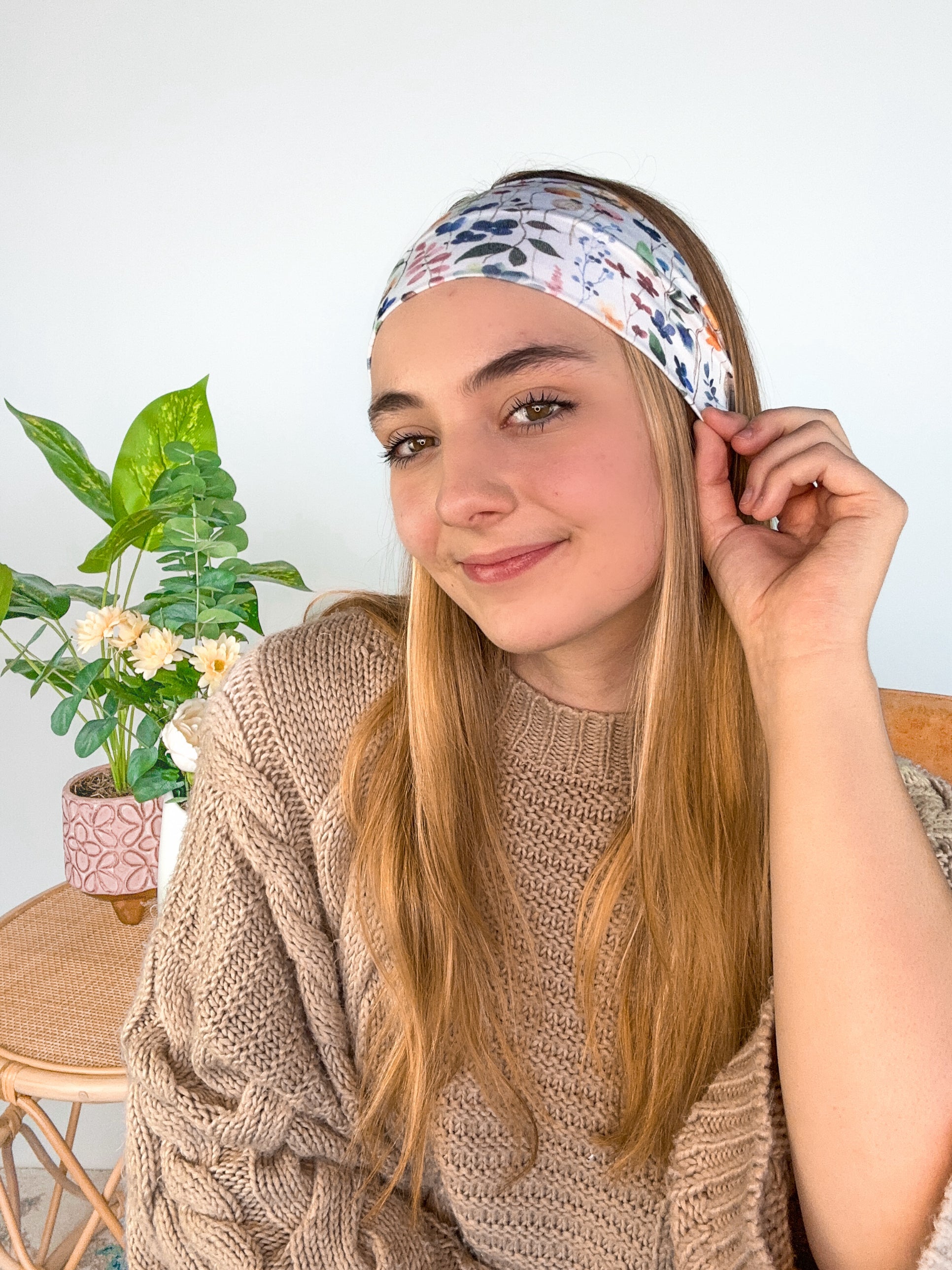 A woman wearing the Alyssa Floral on Ivory headband, showcasing a versatile twist style. Made of soft, stretchy fabric, sweat-absorbent, and non-slip for workouts or play. Designed in Springfield, MO.
