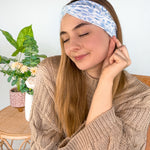 A woman wearing the Olivia Floral on Ivory headband, smiling. Versatile 3-in-1 twist style, machine washable, sweat absorbent, non-slip, designed for confidence and function.