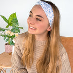 A woman wearing the Olivia Floral on Ivory headband, smiling. Versatile 3-in-1 twist style, machine washable, sweat absorbent, non-slip, designed for confidence and function.