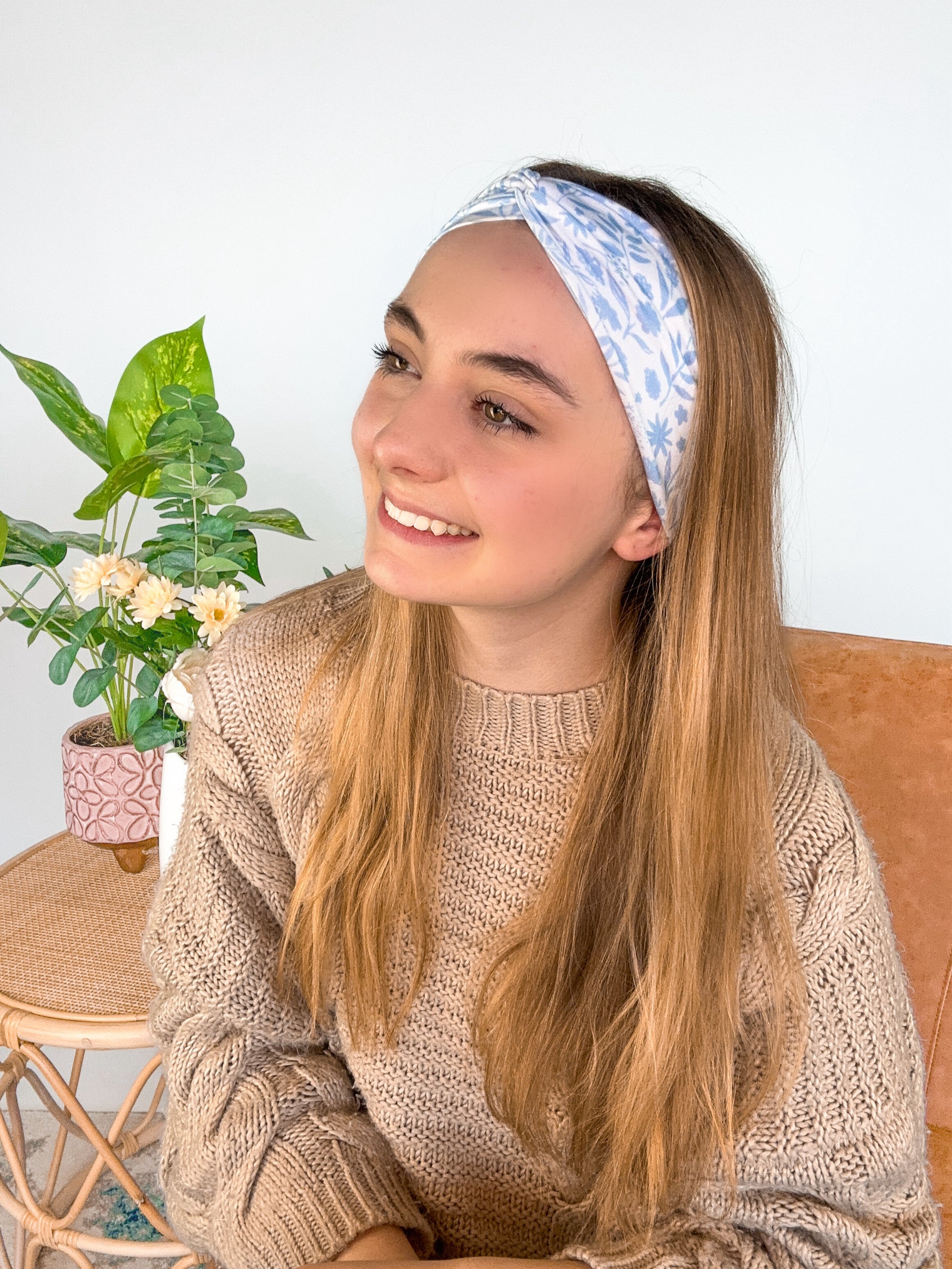 A woman wearing the Olivia Floral on Ivory headband, smiling. Versatile 3-in-1 twist style, machine washable, sweat absorbent, non-slip, designed for confidence and function.