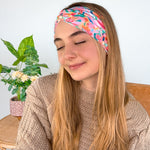 A woman smiling wearing a Kara Floral on Blue headband, showcasing a versatile 3-in-1 twist style. Functional, machine washable, sweat-absorbent, and non-slip for workouts or play. Designed in Springfield, MO.