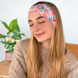 A woman smiling wearing a Kara Floral on Blue headband, showcasing a versatile 3-in-1 twist style. Functional, machine washable, sweat-absorbent, and non-slip for workouts or play. Designed in Springfield, MO.