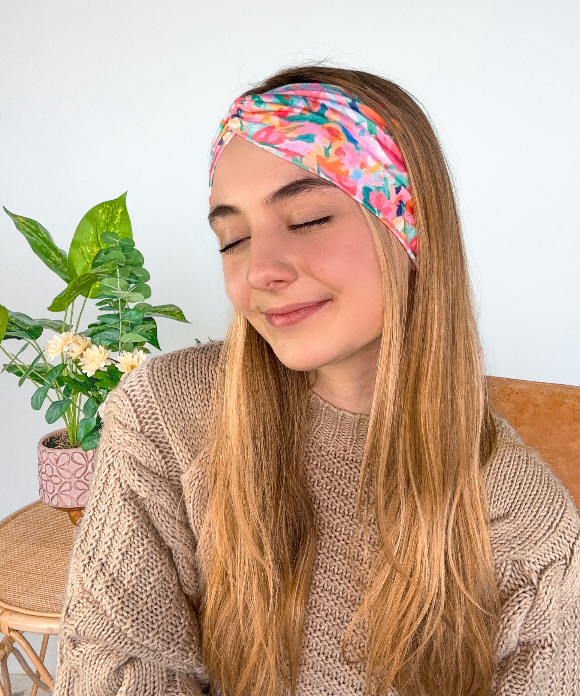 A woman smiling wearing a Kara Floral on Blue headband, showcasing a versatile 3-in-1 twist style. Functional, machine washable, sweat-absorbent, and non-slip for workouts or play. Designed in Springfield, MO.