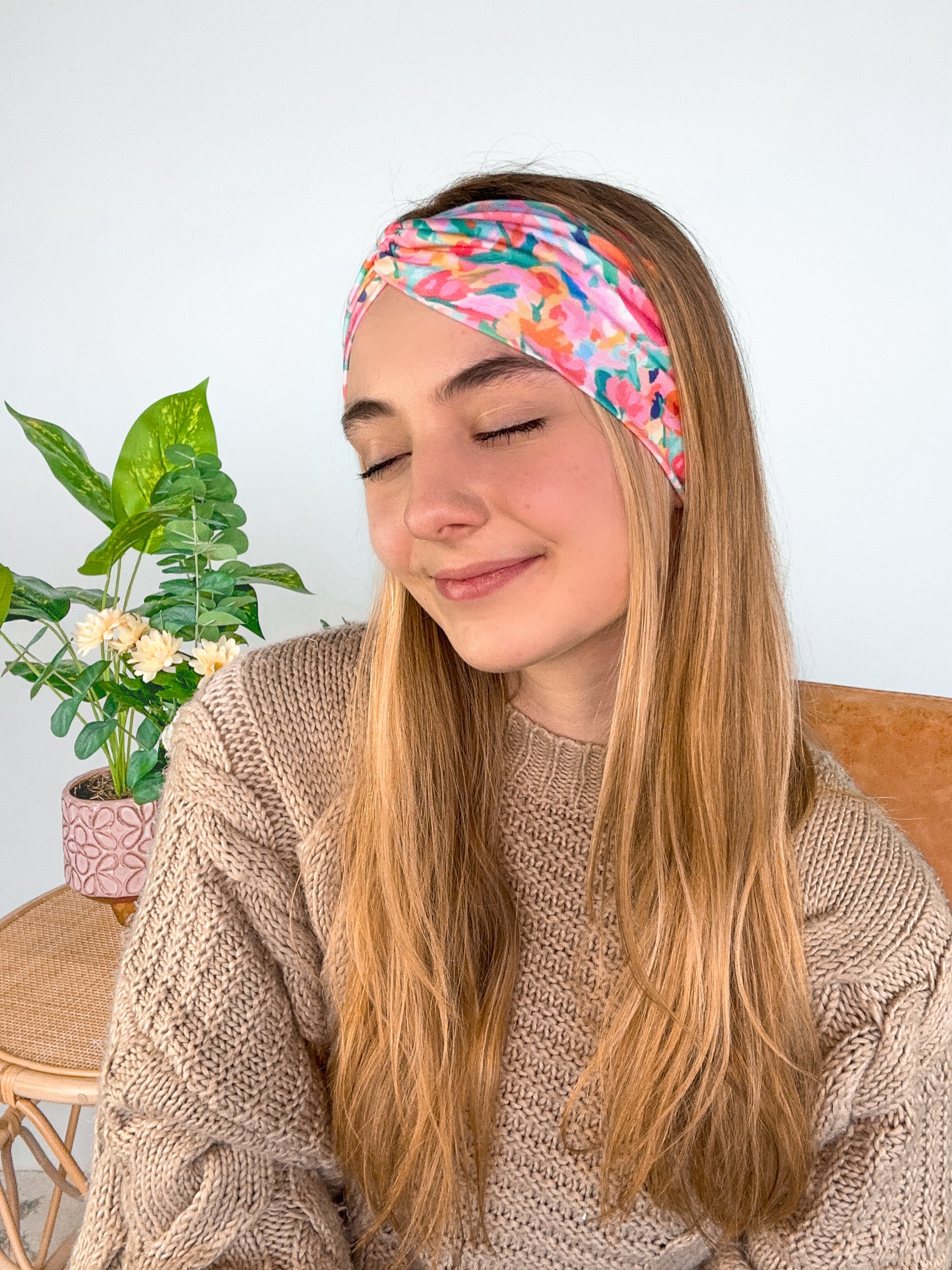 A woman smiling wearing a Kara Floral on Blue headband, showcasing a versatile 3-in-1 twist style. Functional, machine washable, sweat-absorbent, and non-slip for workouts or play. Designed in Springfield, MO.
