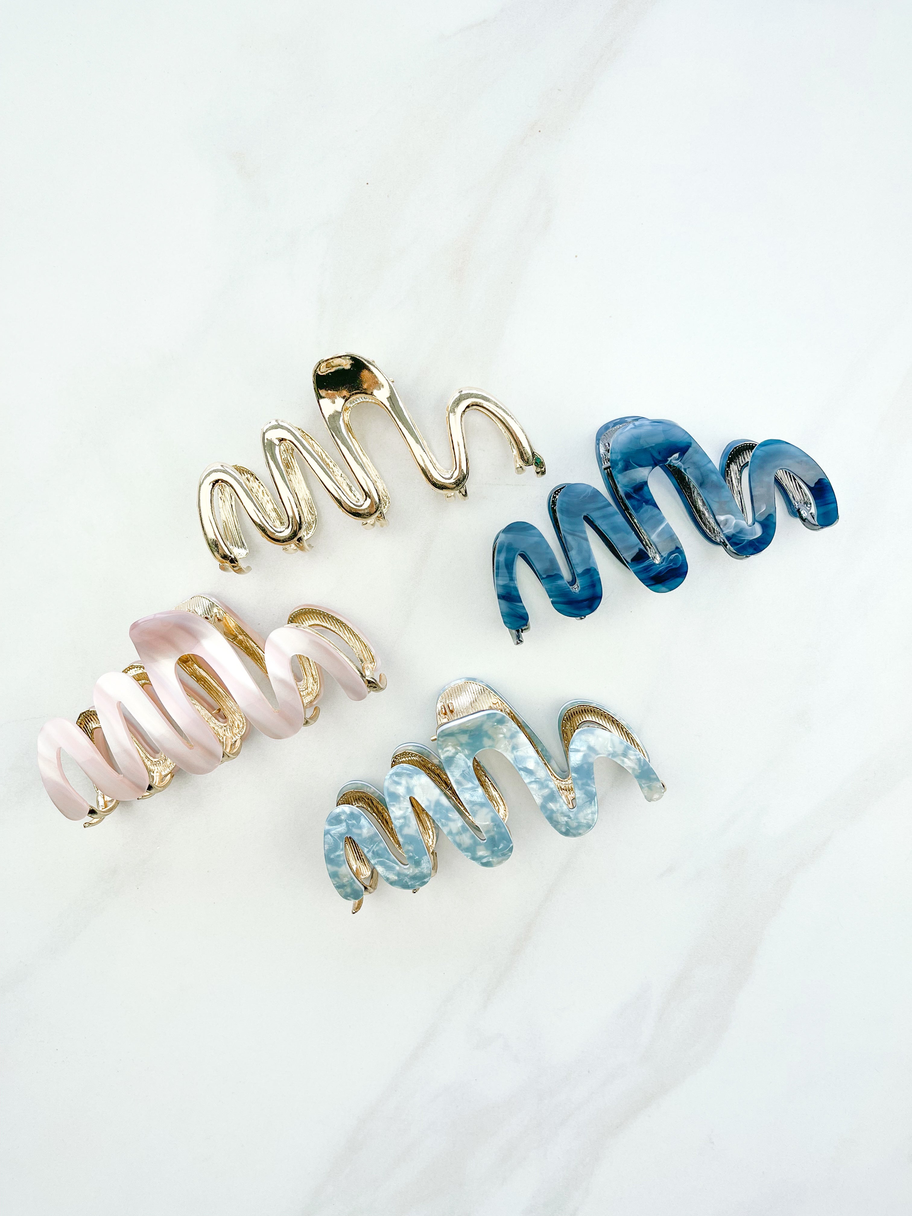 A group of zig zag-shaped marble hair clips with gold trim, including pink, blue, white and dark blue clips and one all-gold clip.