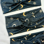 A Dark Side of the Moon headband, showcasing a moon and stars pattern on soft poly-knit fabric. Versatile twist style, sweat-absorbent, and non-slip for workouts or play.