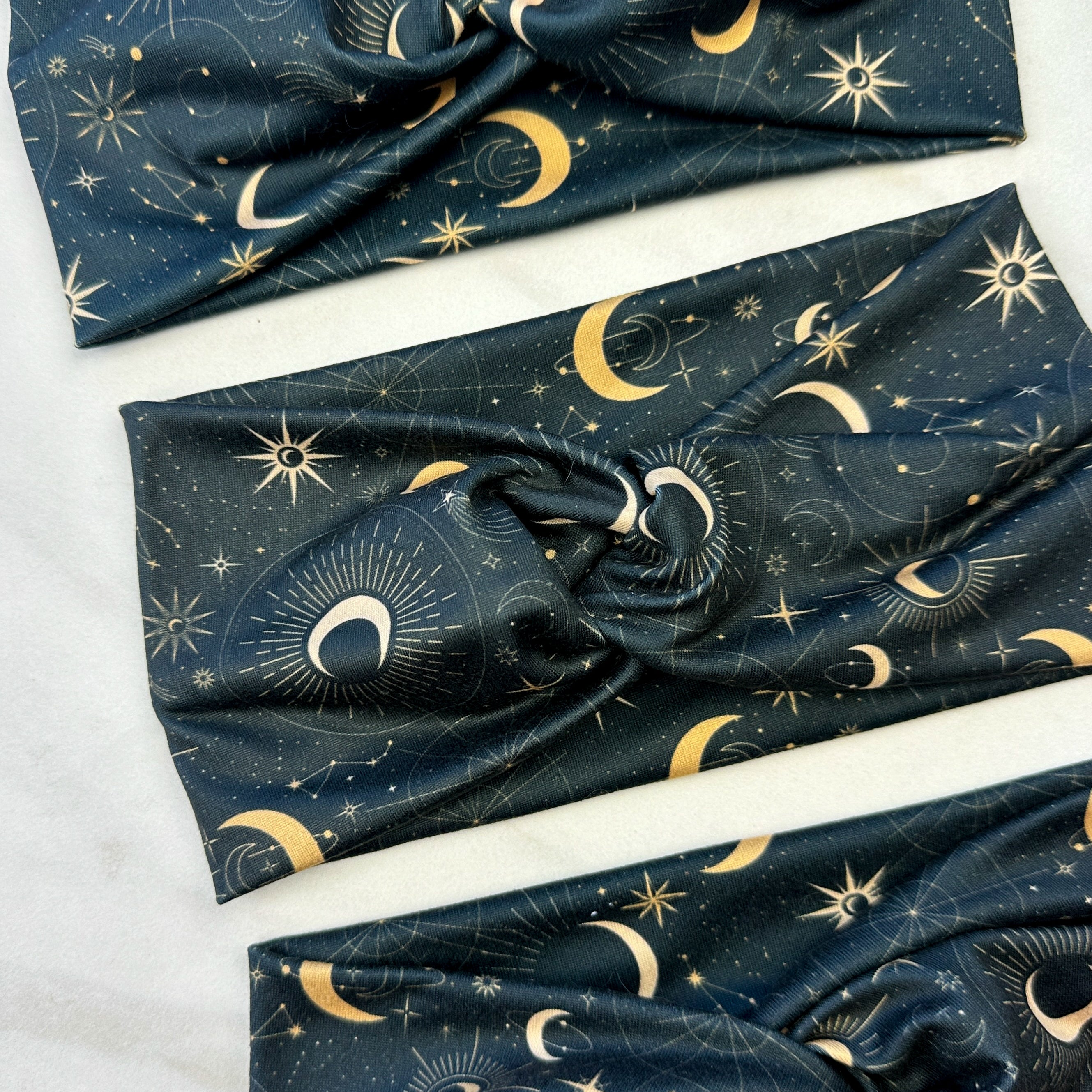 A Dark Side of the Moon headband, showcasing a moon and stars pattern on soft poly-knit fabric. Versatile twist style, sweat-absorbent, and non-slip for workouts or play.