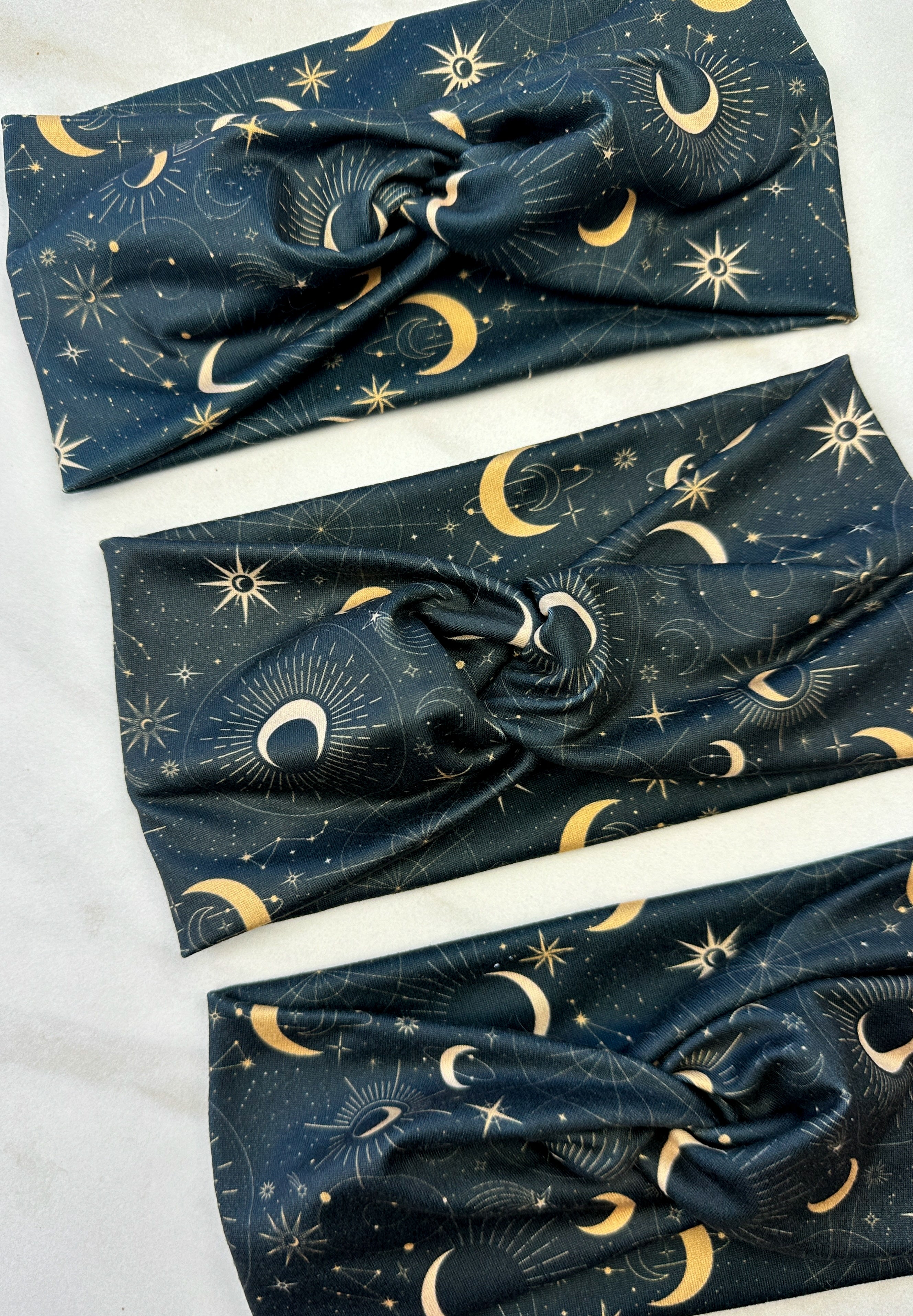 A Dark Side of the Moon headband, showcasing a moon and stars pattern on soft poly-knit fabric. Versatile twist style, sweat-absorbent, and non-slip for workouts or play.