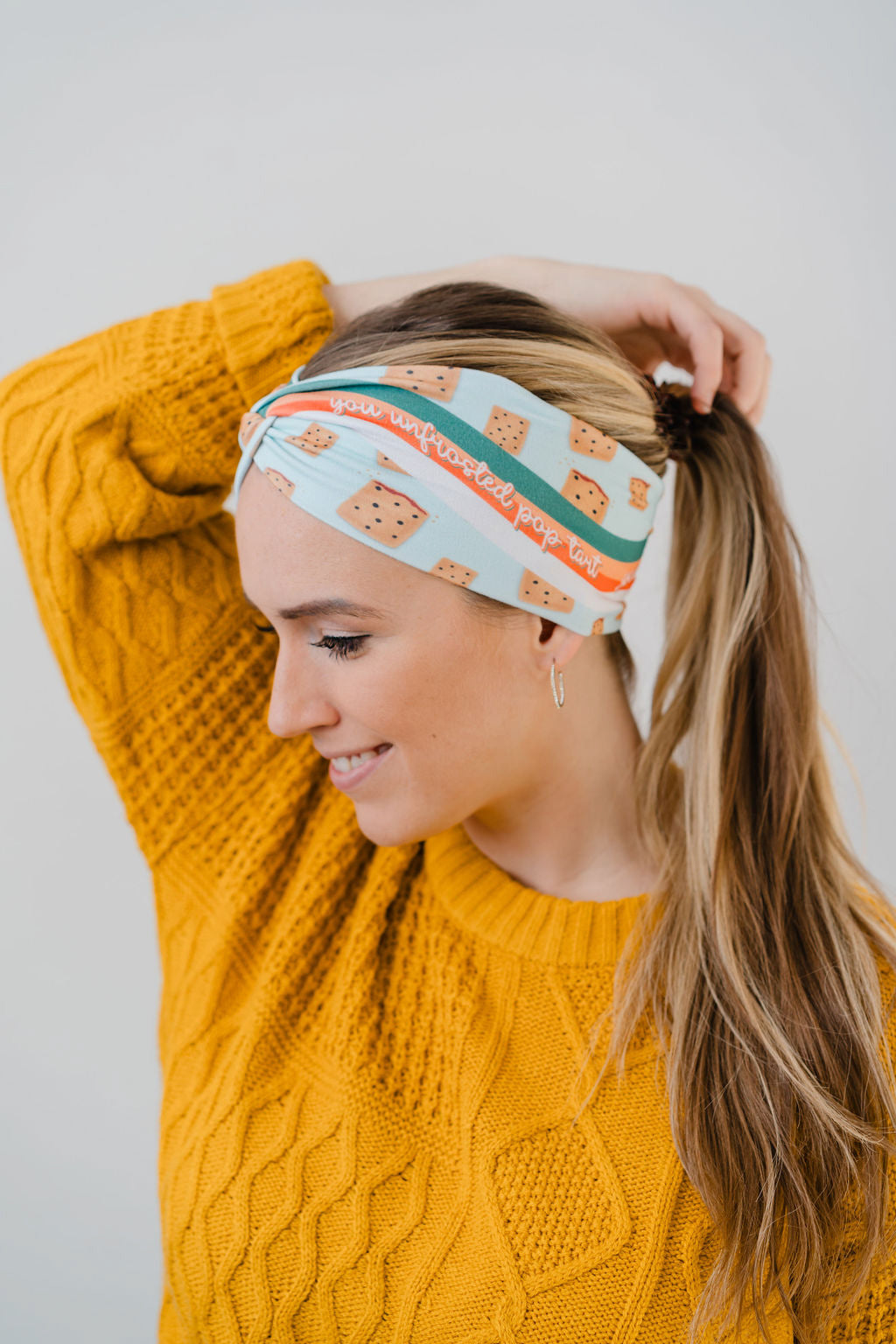 Women wearing the Unfrosted Poptart light blue headband with a wavy rainbow of teal, orange and coral and unfrosted pop-tarts with the words "you unfrosted pop-tart" in cursive