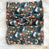 Adult women's black headband with artistic black and white skunk and teal, gold, pink and white allover flowers