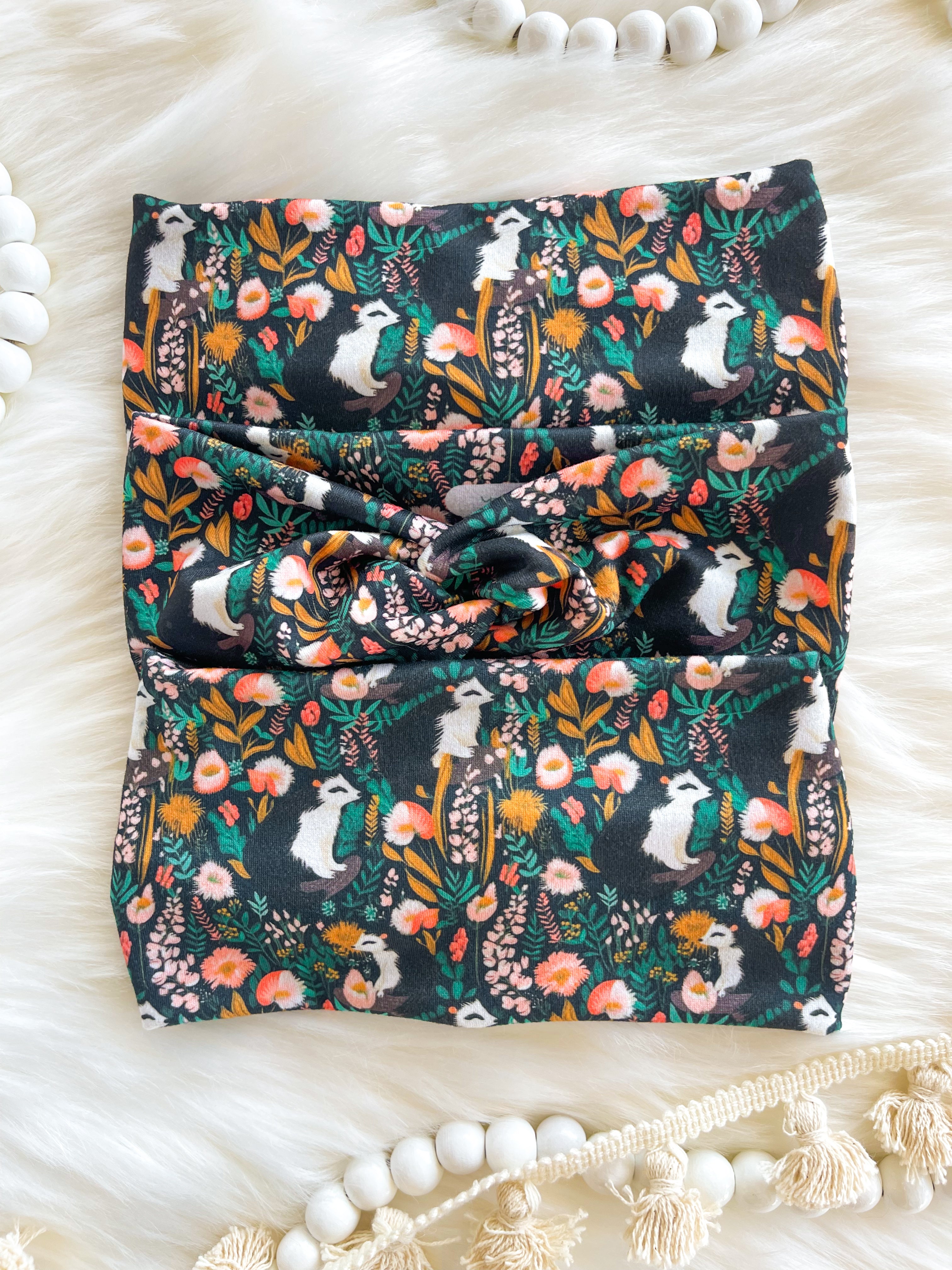 Adult women's black headband with artistic black and white skunk and teal, gold, pink and white allover flowers