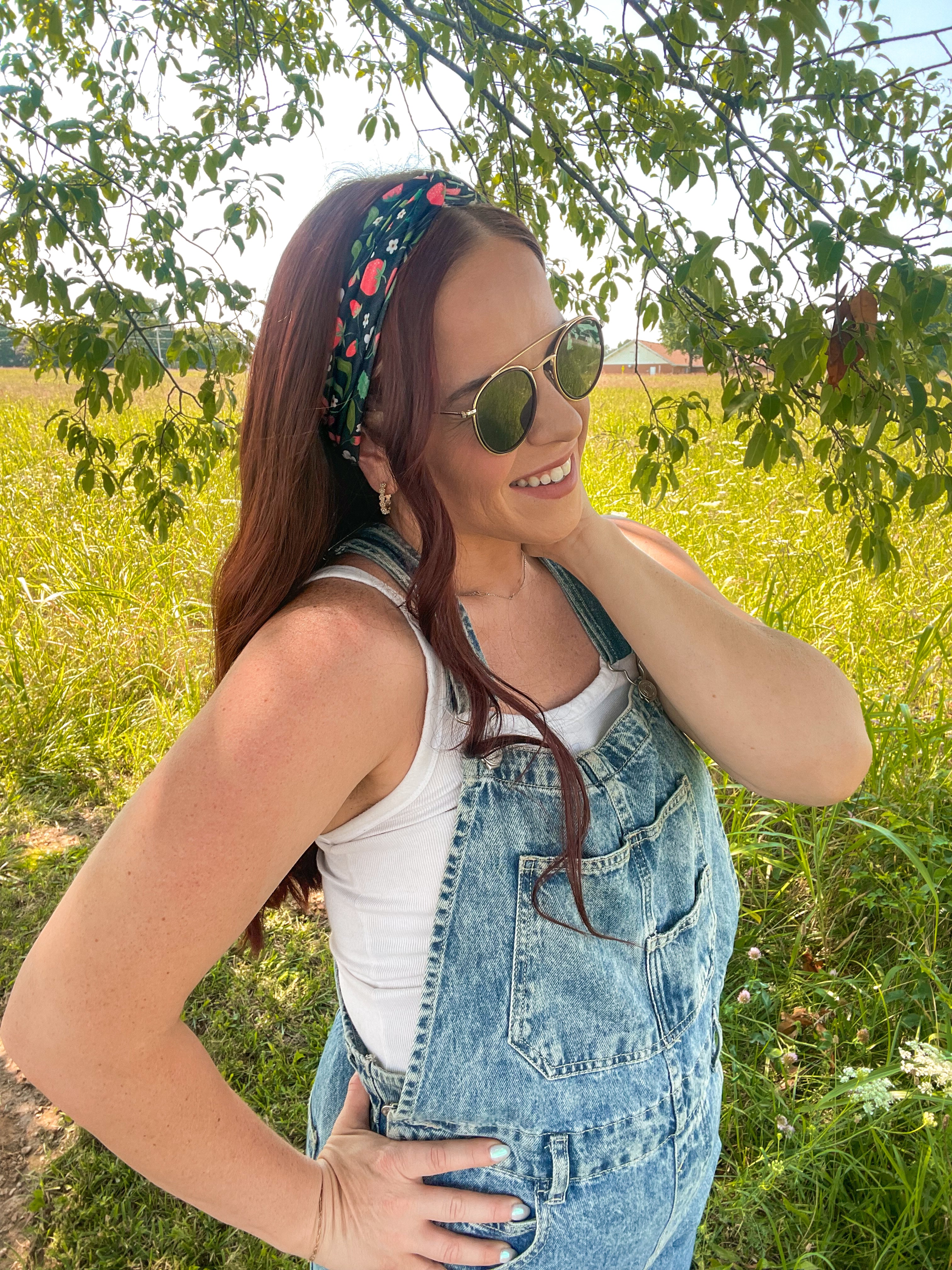 Woman in a field wearing the Feelin' Berry Good headband, sunglasses, and a white tank top with blue overalls, showcasing the headband's stylish functionality.