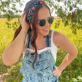 Woman in a field wearing the Feelin' Berry Good headband, sunglasses, and a white tank top with blue overalls, showcasing the headband's stylish functionality.