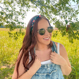 Woman in a field wearing the Feelin' Berry Good headband, sunglasses, and a white tank top with blue overalls, showcasing the headband's stylish functionality.