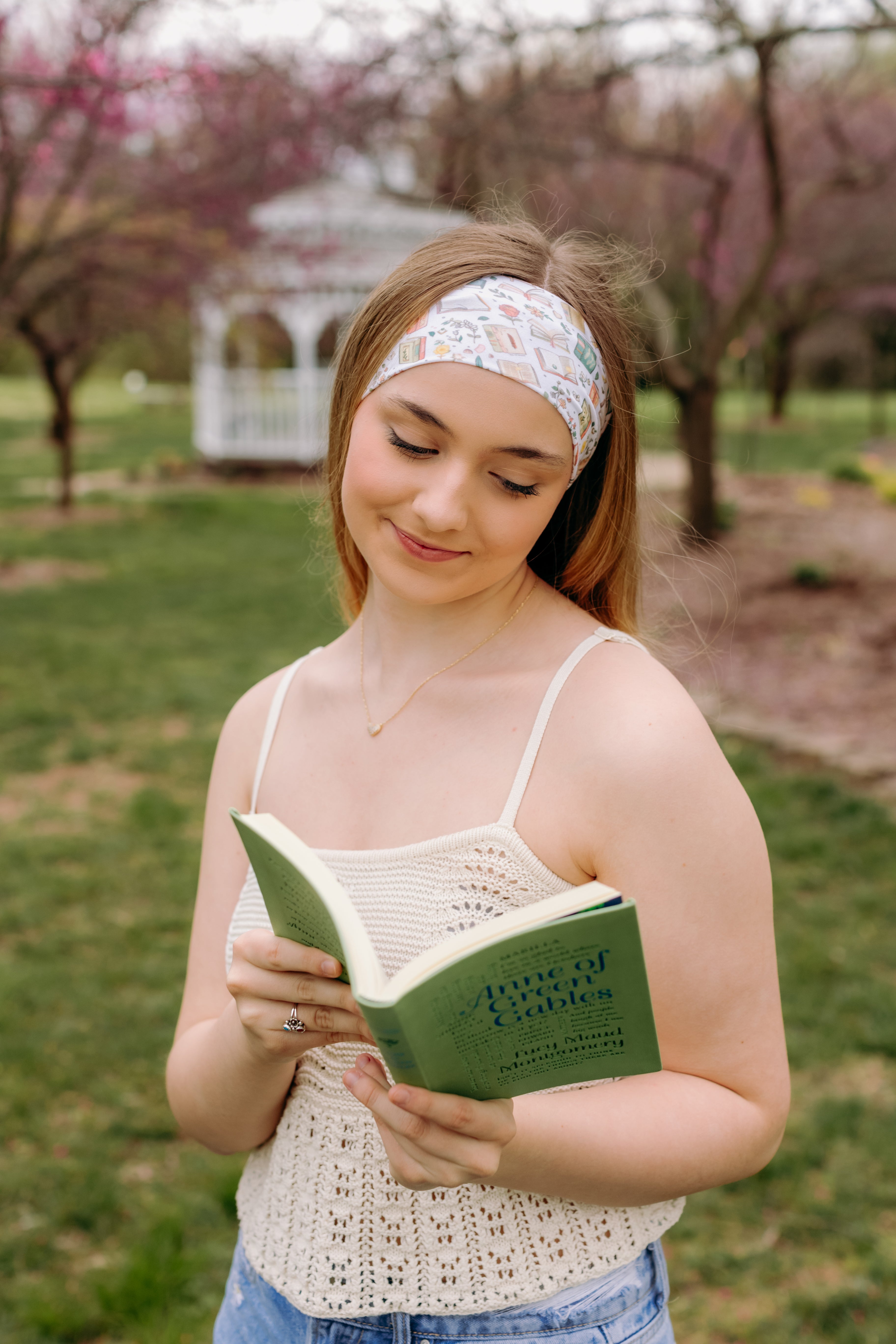 A woman confidently reads a book outdoors, wearing a Petals & Pages Lilac Market Headband. Versatile 3-in-1 twist style, sweat-absorbent, non-slip, machine washable, perfect for workouts or play. Sizes for women and children.