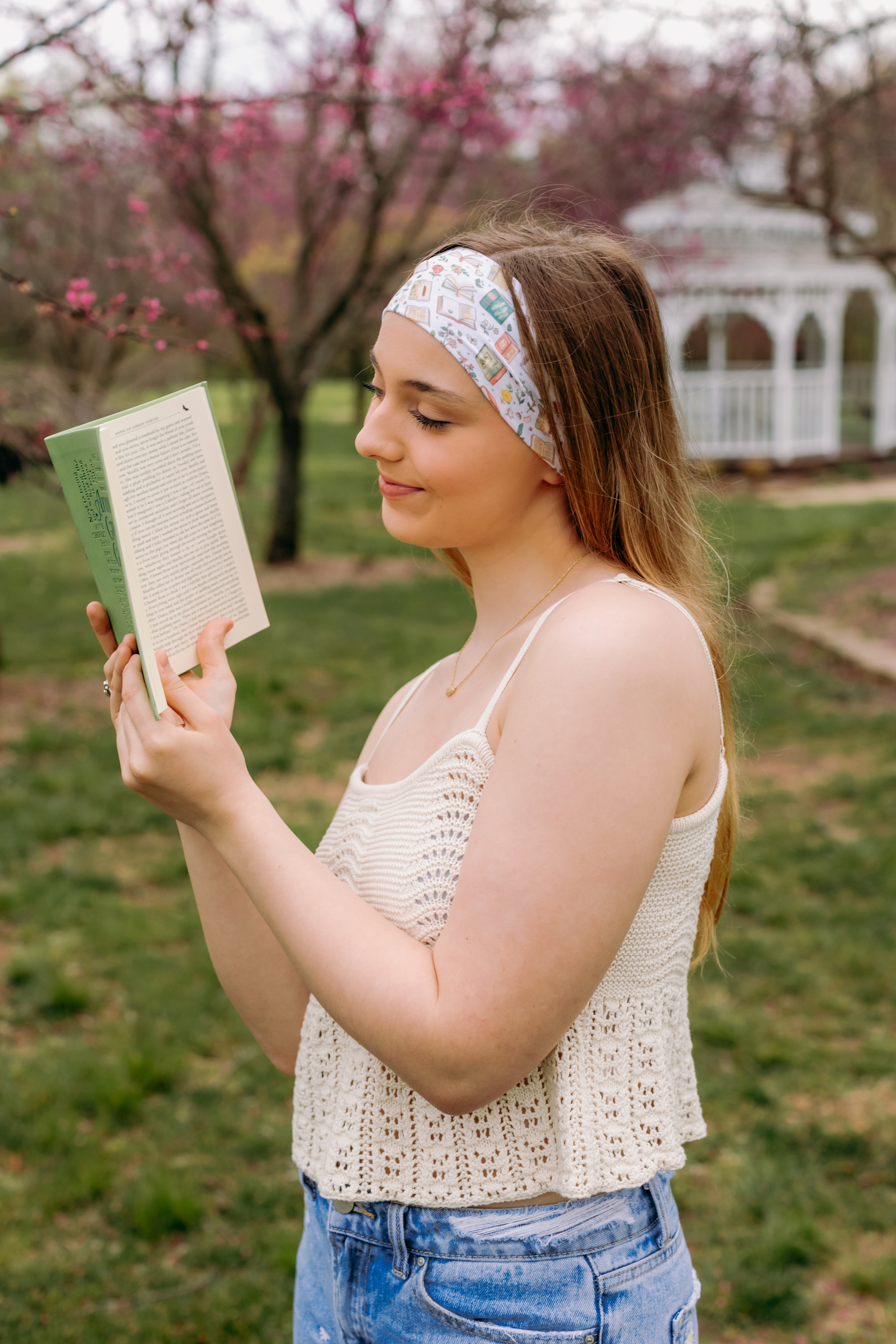 A woman confidently reads a book outdoors, wearing a Petals & Pages Lilac Market Headband. Versatile 3-in-1 twist style, sweat-absorbent, non-slip, machine washable, perfect for workouts or play. Sizes for women and children.