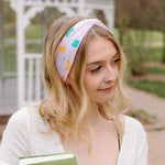 A woman wearing a Book Fairy headband holds books, embodying confidence and functionality. Lilac Market Headbands: versatile, sweat-absorbent, non-slip, perfect for workouts or play. Designed in Springfield, MO.