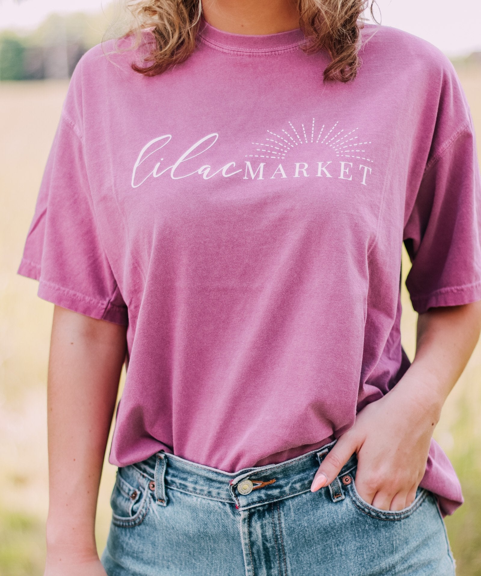 Adult berry colored shirt with Missouri state with the words "Handcrafted with Love in Springfield, MO" over the back, and "Lilac Market in script in the front with the outline of the setting sun