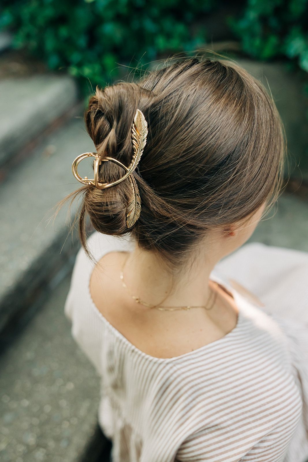 Woman wearing a gold hair clip shaped like a feather in a bun, showcasing the One of a Kind Lilac Clip from The Sarah Wallace Collection.