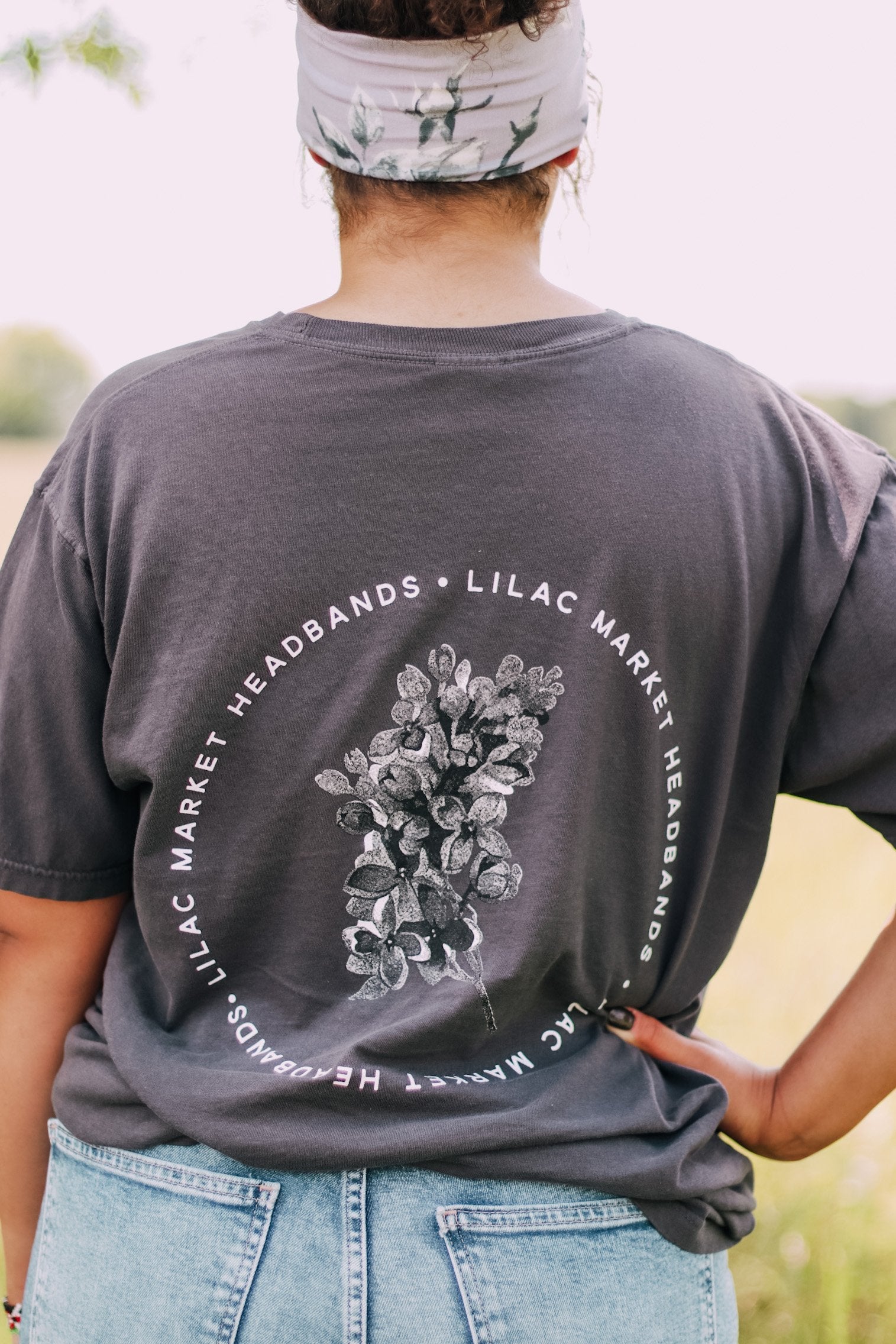 Adult grey colored shirt with grey lilac flowers with the words "Lilac Market Headbands" encircling them, and "Lilac Market" script on the front over a small pocket