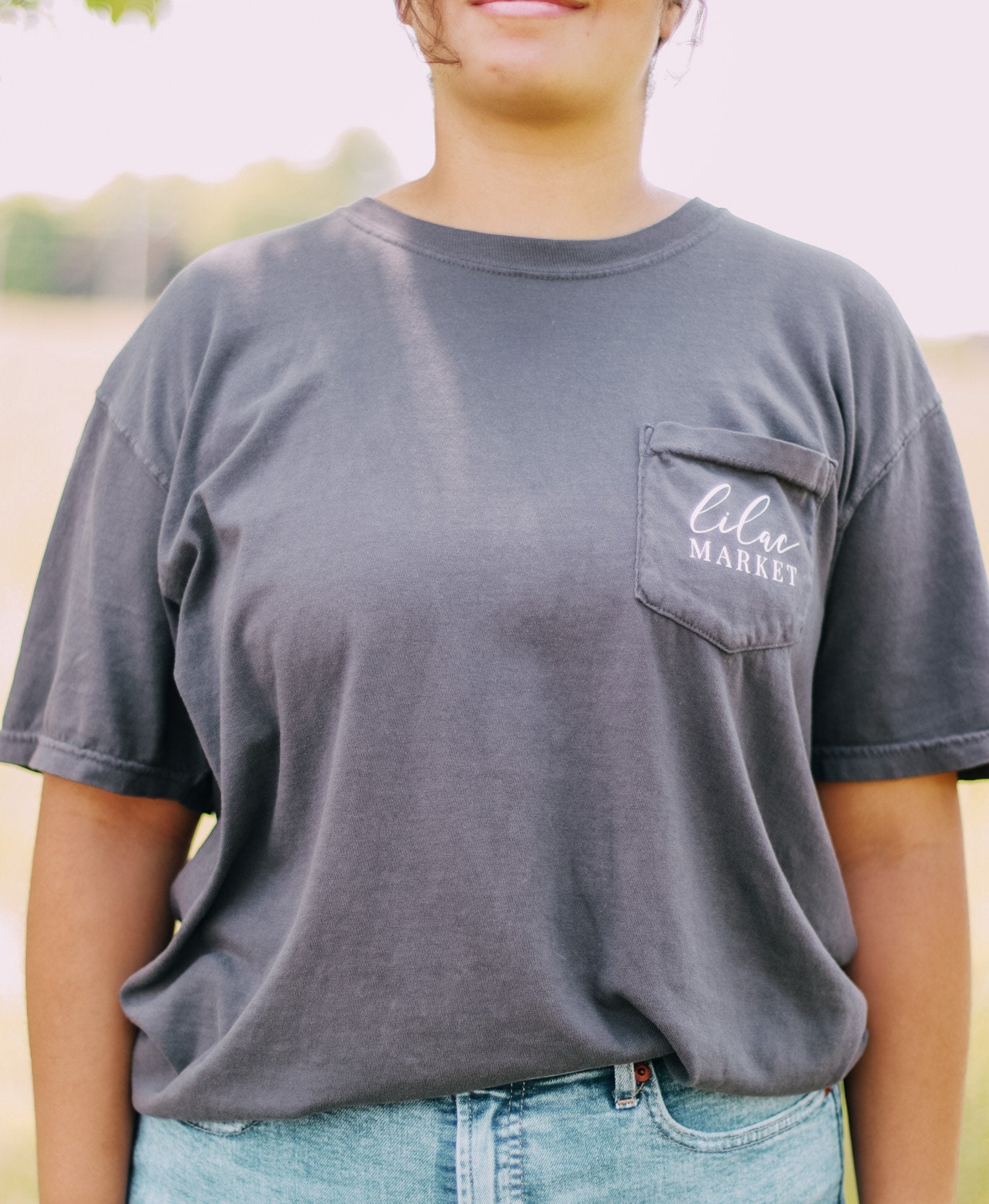 Adult grey colored shirt with grey lilac flowers with the words "Lilac Market Headbands" encircling them, and "Lilac Market" script on the front over a small pocket