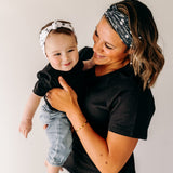 A woman smiles, holding a baby, wearing a twist knot I'm a Cool Mom - Mommy & Me headbands, adjustable for babies and toddlers. Designed in Springfield, MO.