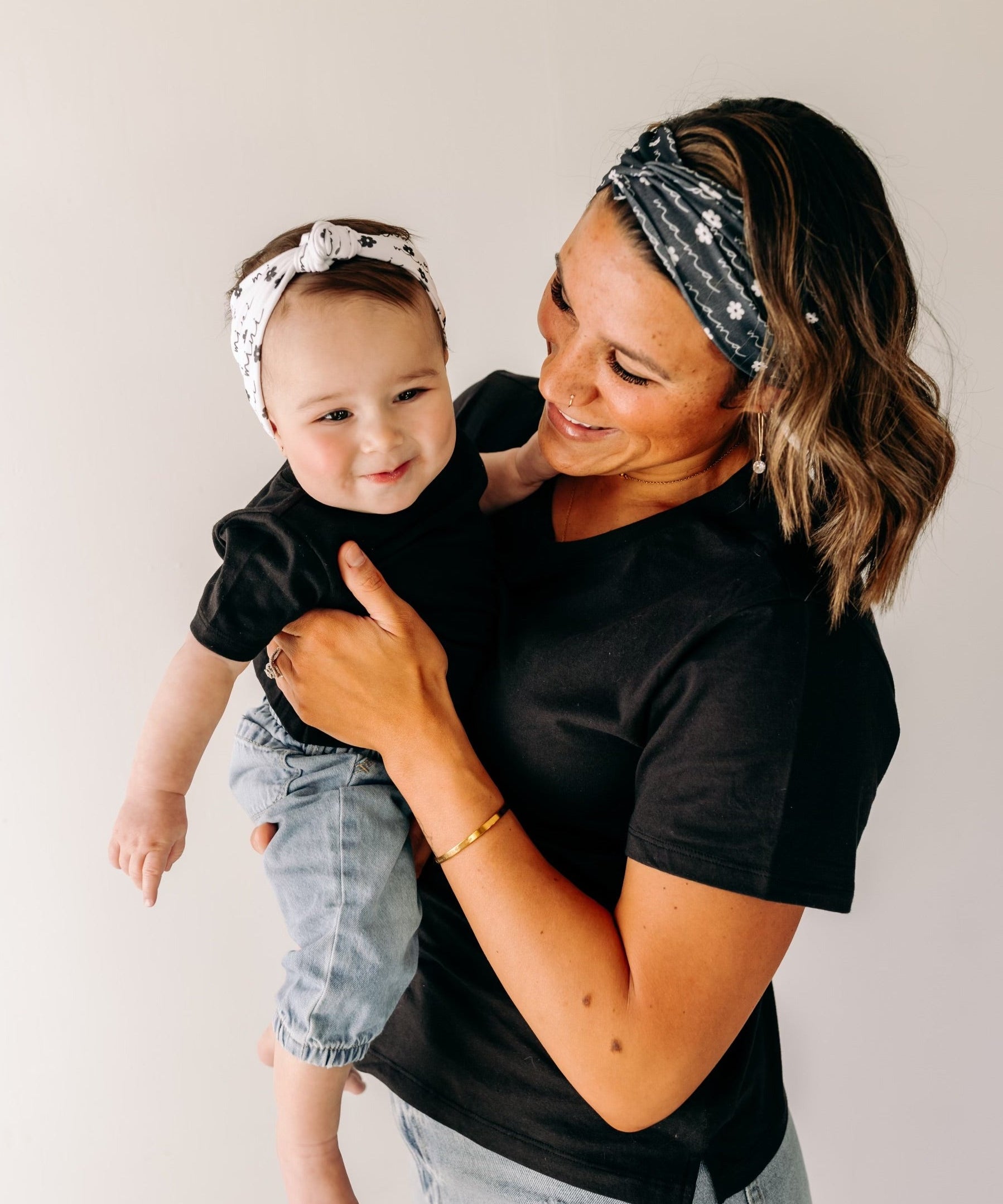 A woman smiles, holding a baby, wearing a twist knot I'm a Cool Mom - Mommy & Me headbands, adjustable for babies and toddlers. Designed in Springfield, MO.